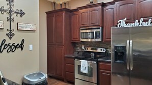 A kitchen with wooden cabinets, a stainless steel refrigerator, a microwave, and an oven. There are decorative wall hangings and a trash can. - Cozy 2-bedroom house in Harlingen BBQ grill and back patio. (Harlingen)