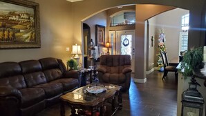 A living room with a brown leather sofa, a wooden coffee table, and a dark armchair. There is a painting on the wall and a Christmas tree in the background. - Cozy 2-bedroom house in Harlingen BBQ grill and back patio. (Harlingen)