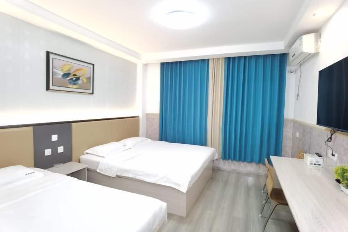 Quarto de hotel com duas camas, uma escrivaninha, uma cadeira, televisão e janela com cortinas.