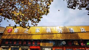 Ein Hotel mit einem Schild in chinesischen Schriftzeichen, eine Ladenzeile mit verschiedenen Geschäften und ein Baum mit Herbstlaub.