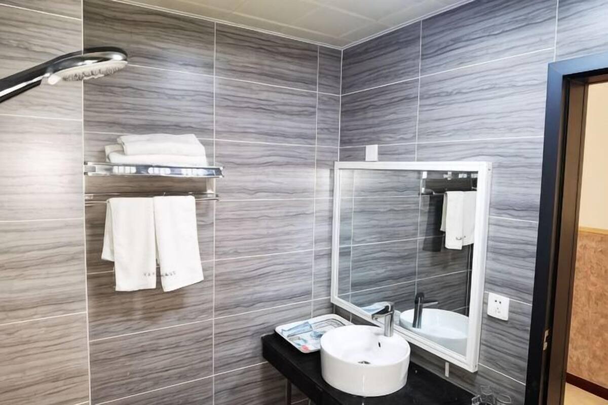 Um banheiro moderno com azulejos cinzas, pia branca, espelho e chuveiro.