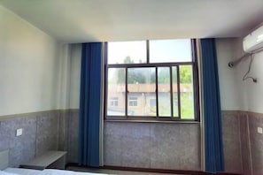 Una habitación con una cama, una ventana con cortinas azules y un equipo de aire acondicionado en la pared.