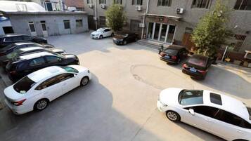 Un estacionamiento con varios autos, un edificio de fachada plana y un árbol en primer plano.