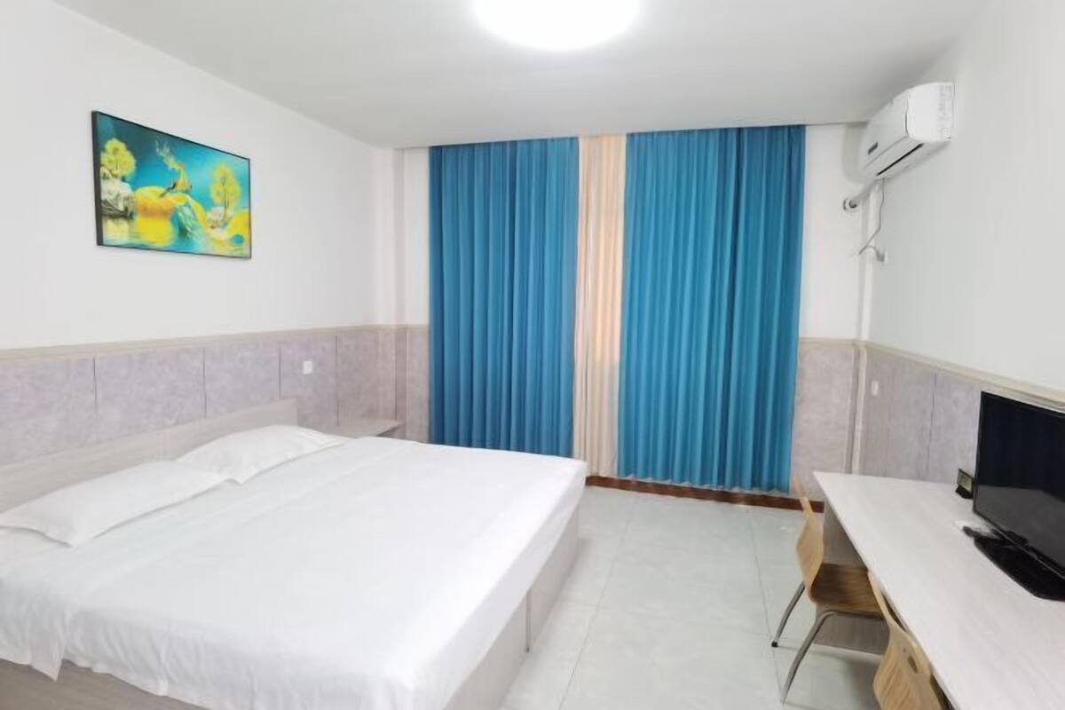 Quarto de hotel com cama, escrivaninha, cadeira, ar condicionado e um quadro na parede.