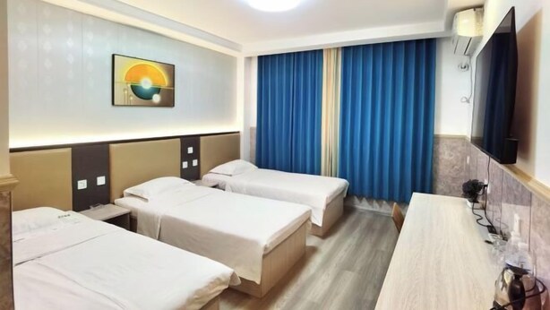 Habitación de hotel con tres camas individuales, un escritorio, un televisor de pantalla plana y un cuadro en la pared.