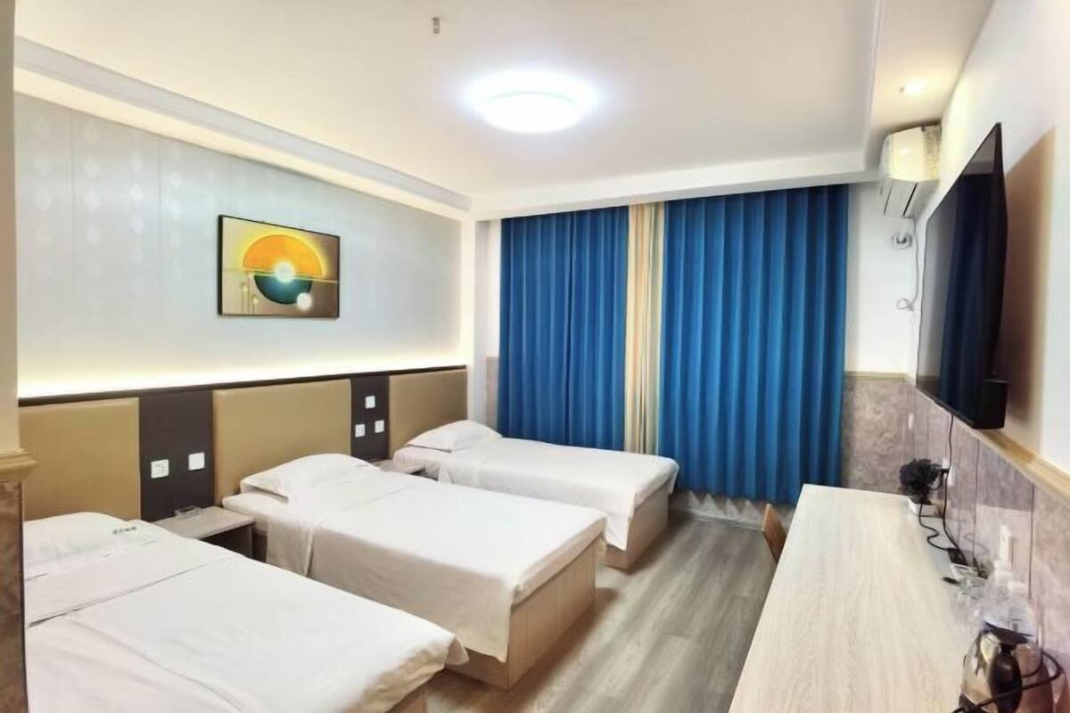 Quarto de hotel com três camas de solteiro, uma escrivaninha, televisão de tela plana e um quadro na parede.