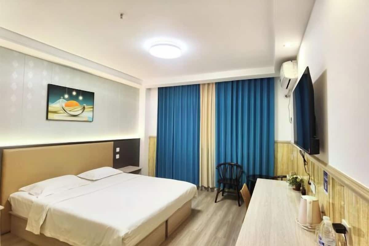 Quarto de hotel com cama, escrivaninha, cadeira, televisão e janela com cortinas.
