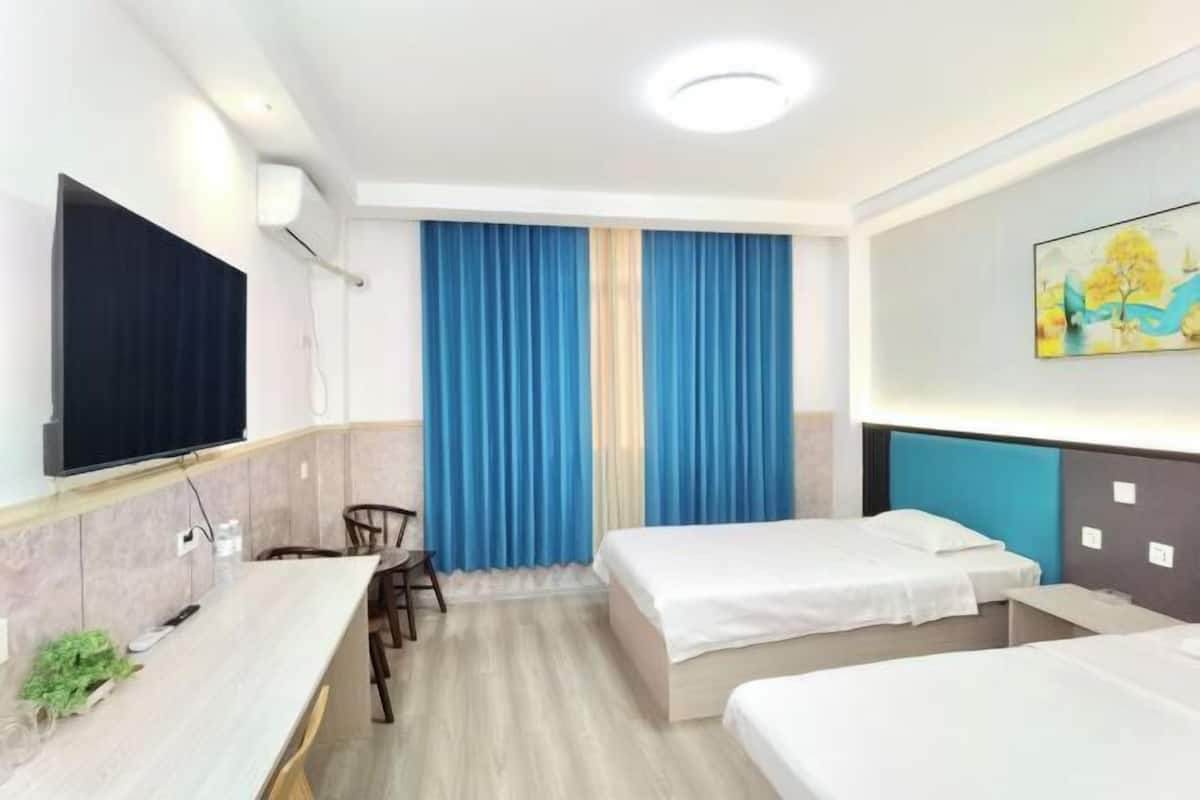 Quarto de hotel com uma cama, uma secretária, uma cadeira, uma televisão e um quadro na parede.