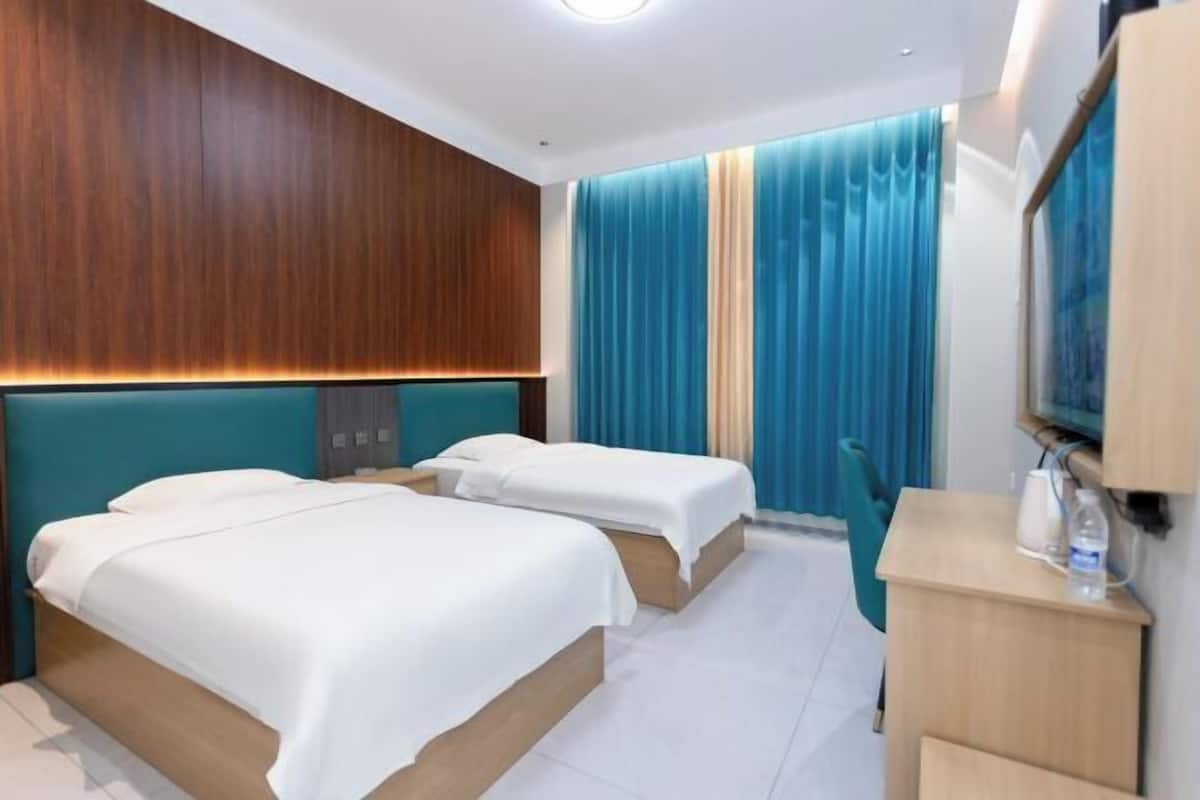 Quarto de hotel com duas camas, cabeceira de madeira, escrivaninha com cadeira e televisão.