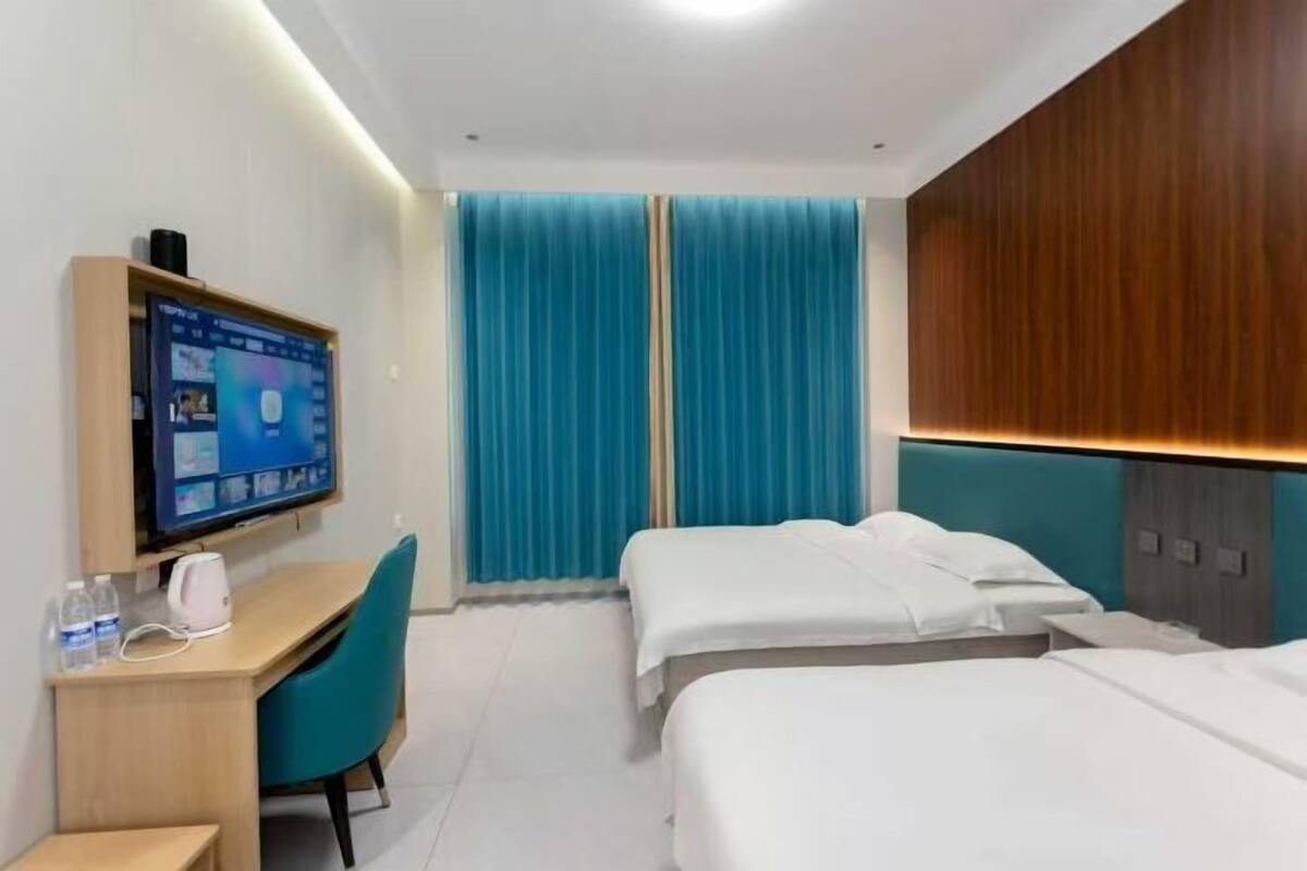 Quarto de hotel com escrivaninha, duas camas, televisão e cortina azul.