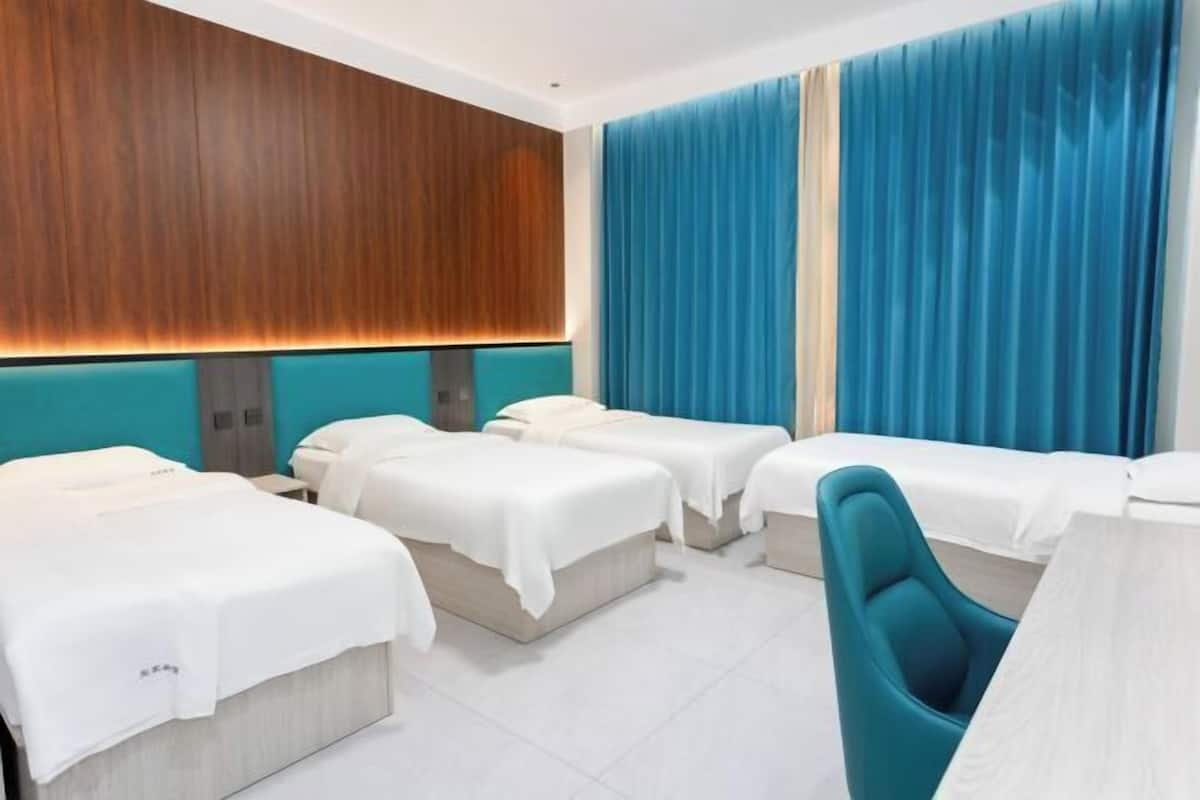 Quarto de hotel com três camas, uma escrivaninha e uma cadeira.