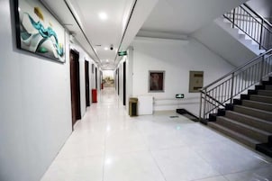 Un pasillo de hotel con una escalera, un bote de basura y un cuadro en la pared.