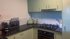 A kitchen with light green cabinets, a black countertop, a coffee maker, a toaster, and a stove. - Leaf Luxe - 9 Pools BBQ Gym (Cairns)