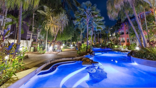 A nighttime resort pool area with palm trees and a water feature. - Leaf Luxe - 9 Pools BBQ Gym (Cairns)