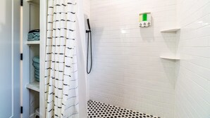 Un baño con paredes de azulejos blancos, una ducha con cabezal de ducha tipo lluvia negro y un suelo con estampado.