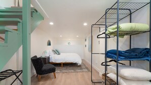Habitación de hotel compacta con una cama litera, una cama individual, una silla y una escalera.