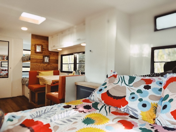 Una habitación acogedora con cama, una mesita y una silla. Se ve una ventana con vistas a árboles.
