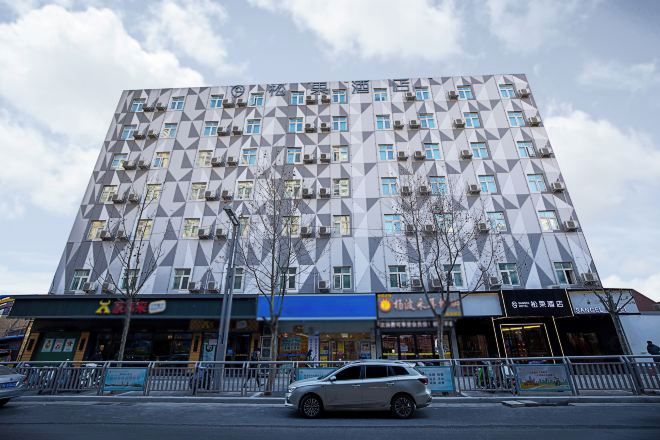 A multi-story building with a geometric facade, featuring a series of windows and air conditioning units.