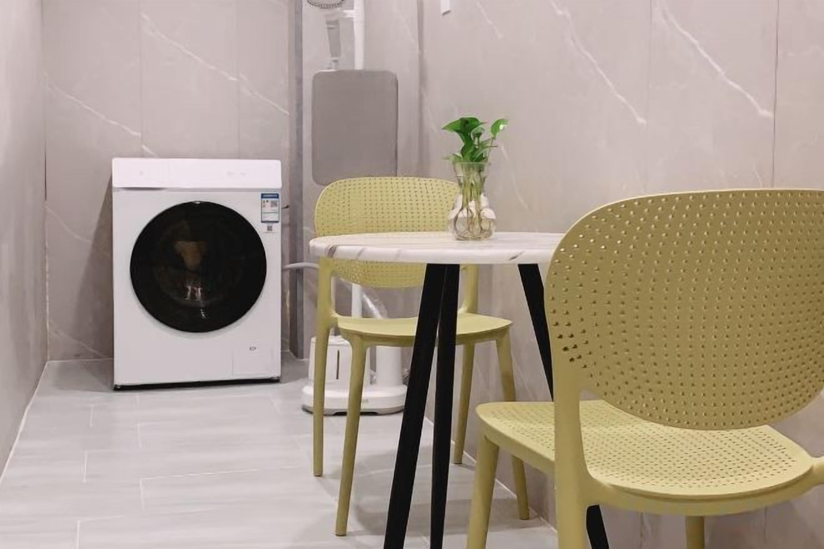 Ein kleines Badezimmer mit Waschmaschine, einem Tisch, zwei Stühlen und einem Blumentopf.