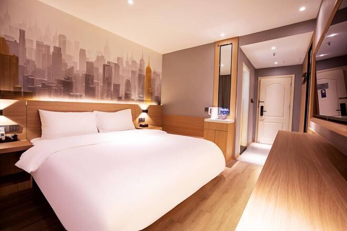 Habitación de hotel con una cama grande, un mural de la ciudad, un cabecero de madera, una mesita de noche y un espejo.