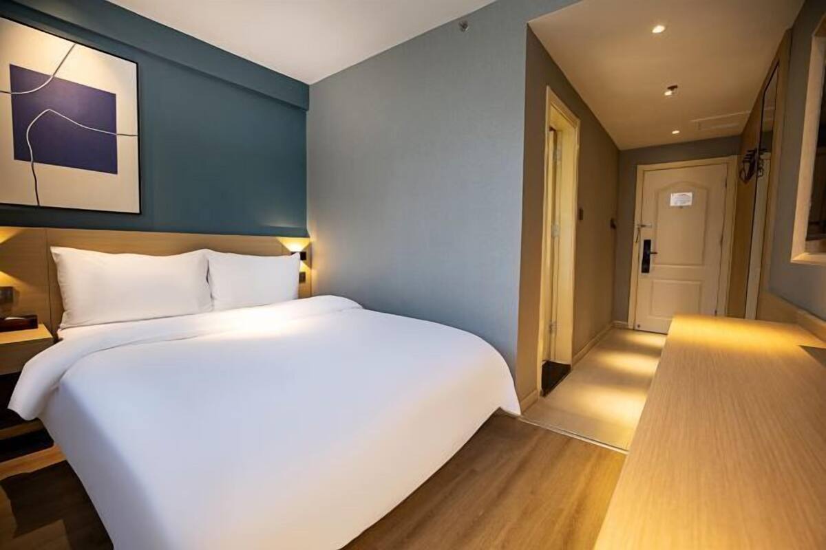 Habitación de hotel con una cama, una mesita de noche, una obra de arte colgada en la pared y una puerta que da a otra habitación.