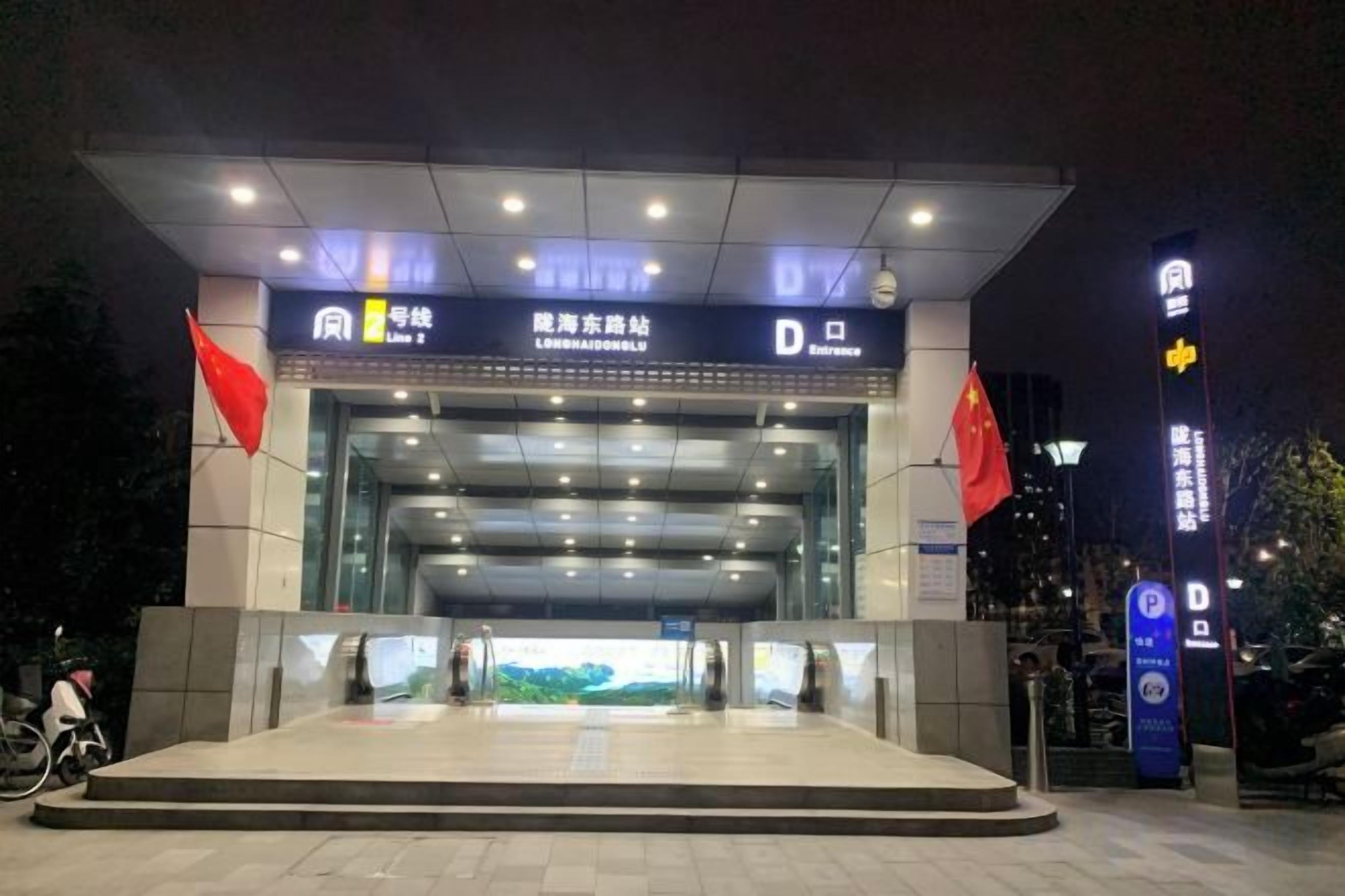 A modern building entrance with a large glass facade, a prominent sign above the entrance, and two flags on either side.