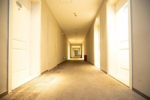 A long, narrow hotel corridor with doors on both sides, carpeted floors, and a light source at the end. - Sangel Hotel (Zhengzhou East Longhai Road Metro Station) (Zhengzhou)