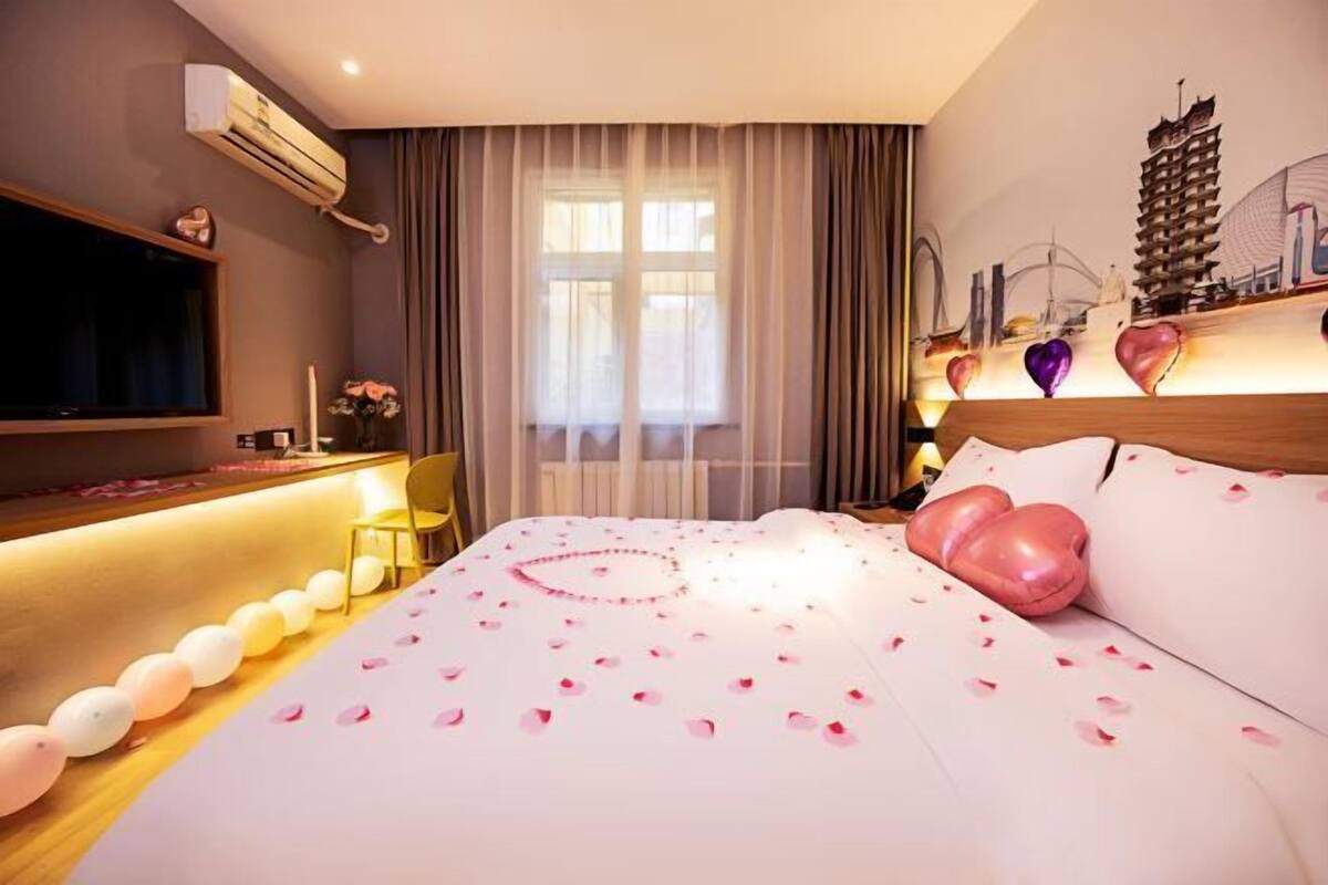 Habitación de hotel con cama, televisión, escritorio con silla y ventana con cortinas.
