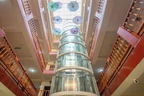 A multi-level atrium with a central glass elevator shaft, wooden railings, and a ceiling with multiple umbrellas. - Holiday Inn Lijiang Langtai (Lijiang)