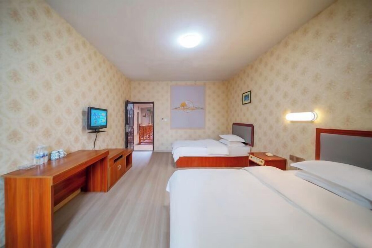 A hotel room with a wooden desk, two beds, a television, and a painting on the wall.