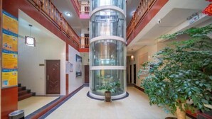 A hotel lobby with a central elevator, a staircase on the left, and a large potted plant on the right. - Holiday Inn Lijiang Langtai (Lijiang)