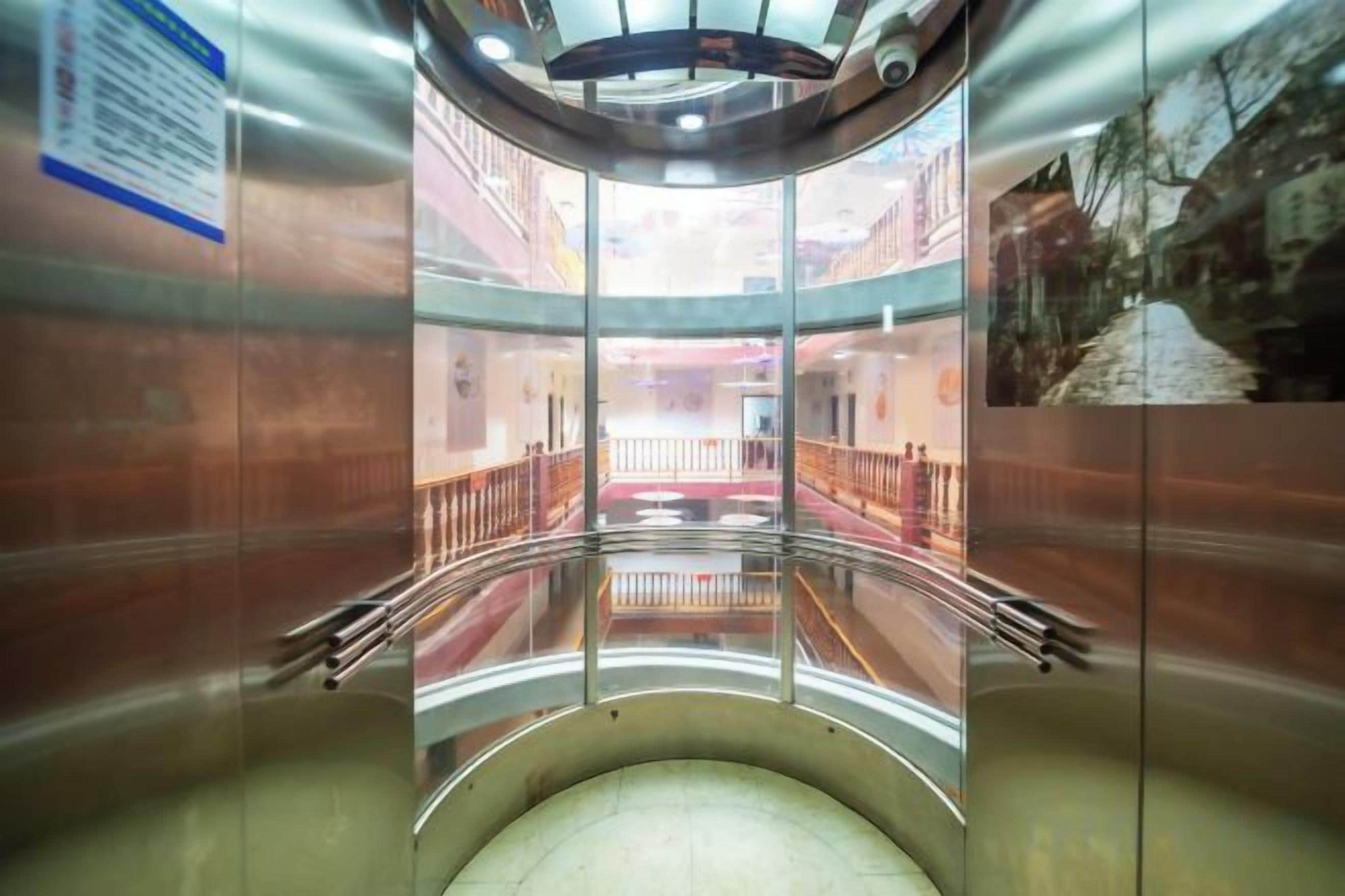 A circular elevator with a glass enclosure, a metal railing, and a view of a building's interior.