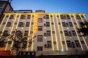 A multi-story hotel building with illuminated vertical lines on the facade, multiple windows, and a sign with Chinese characters. - Holiday Inn Lijiang Langtai (Lijiang)