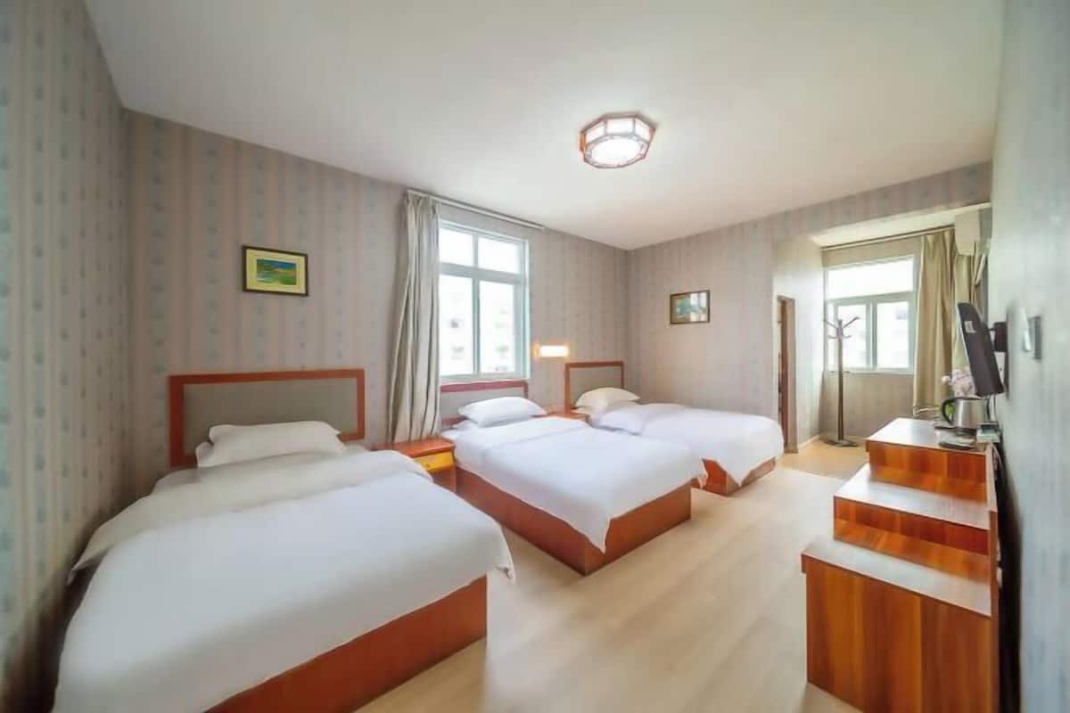 Una habitación de hotel con tres camas, un escritorio de madera y un ventanal grande.