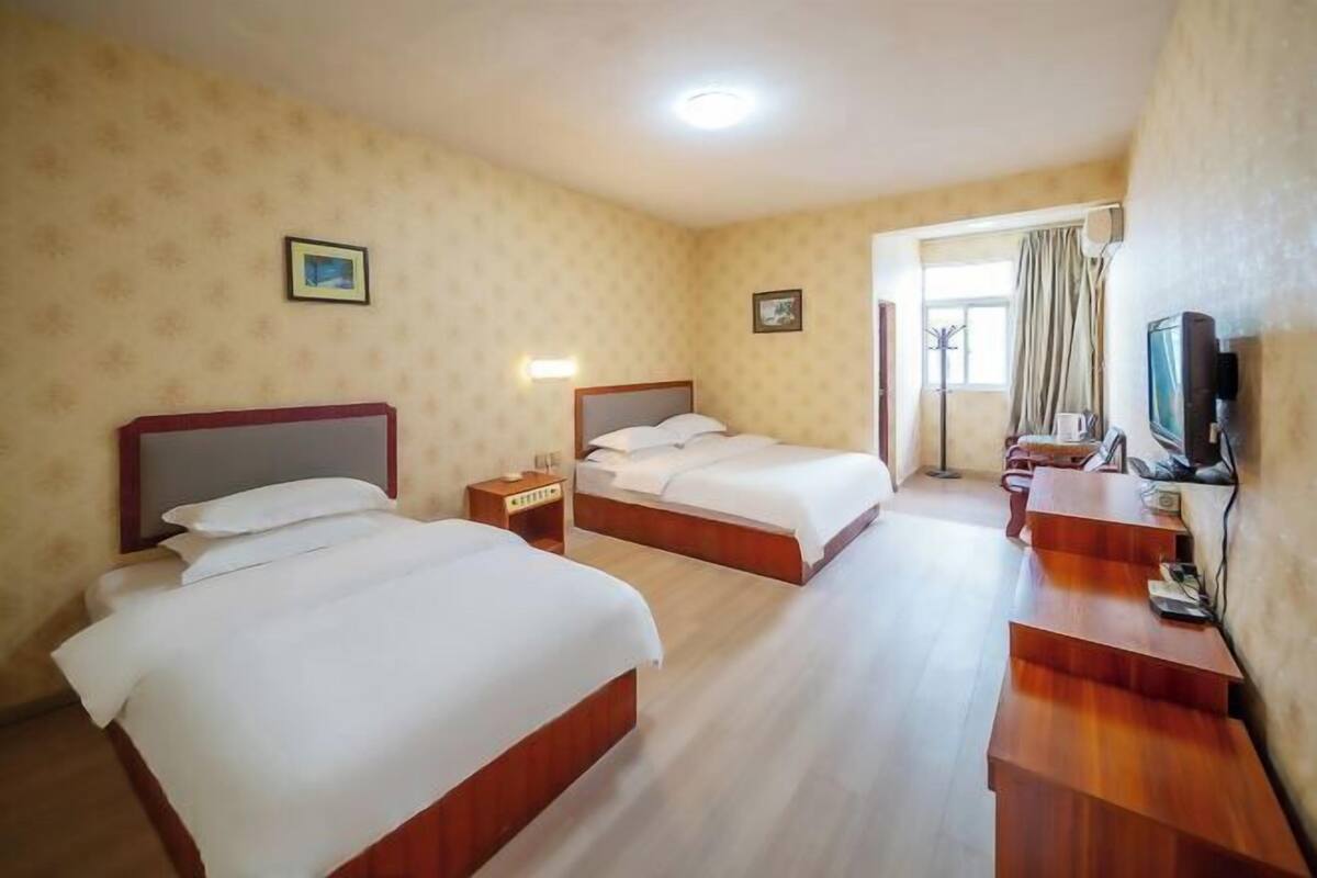 Habitación de hotel con dos camas, televisor, escritorio y ventana con cortinas.