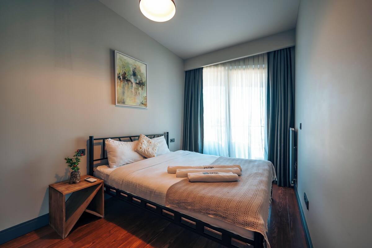 Un dormitorio moderno con estructura de cama de madera, una mesita de noche con una planta y un cuadro en la pared.