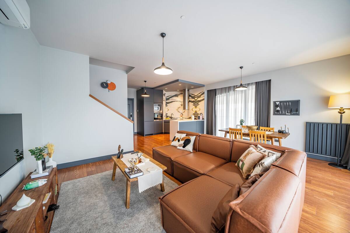 Una sala de estar moderna con un sofá de cuero marrón, una mesa de centro de madera y un comedor con mesa y sillas.