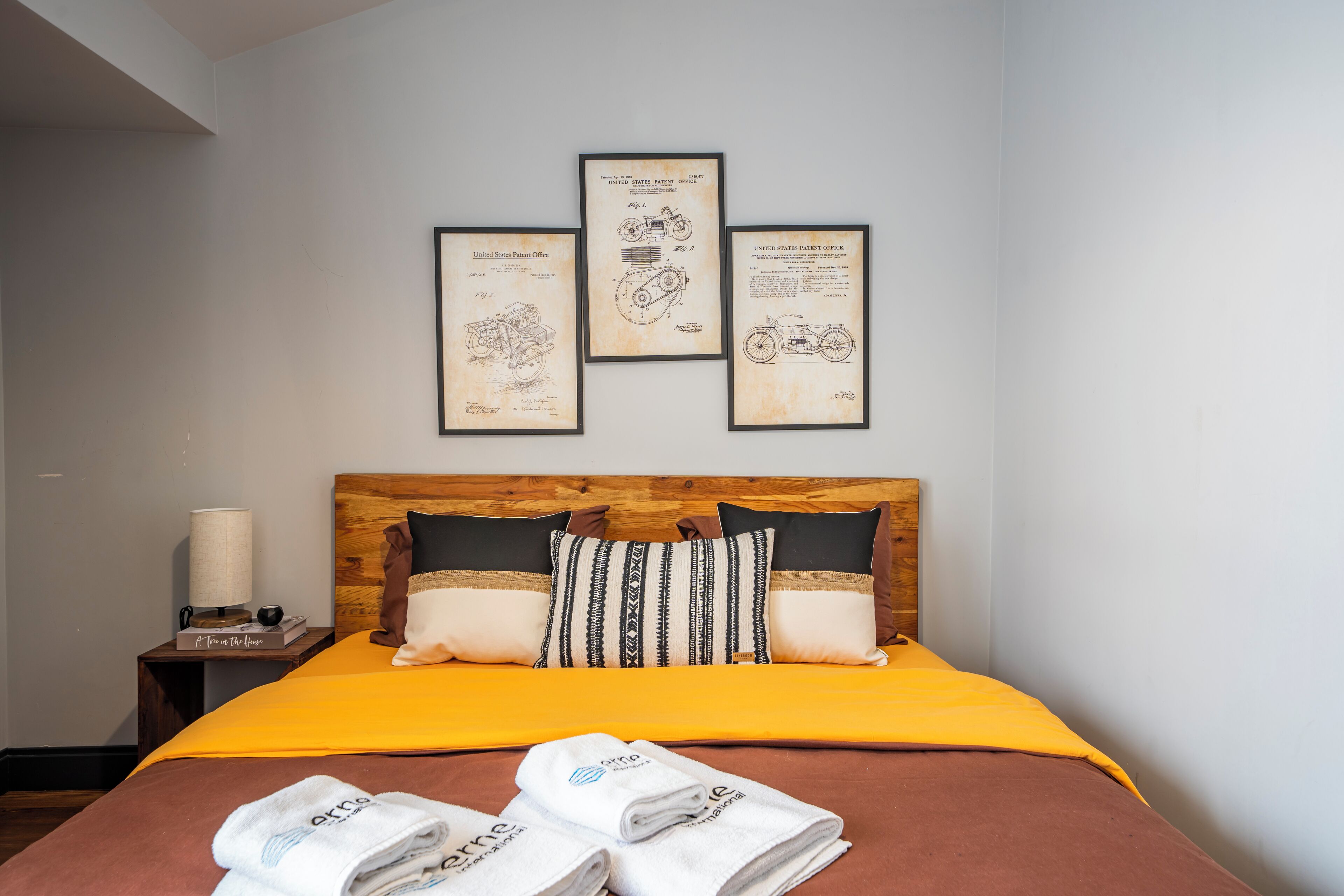 Un lit bien fait, avec une tête de lit en bois, une couvre-lit jaune et trois documents de brevets encadrés accrochés au mur au-dessus.