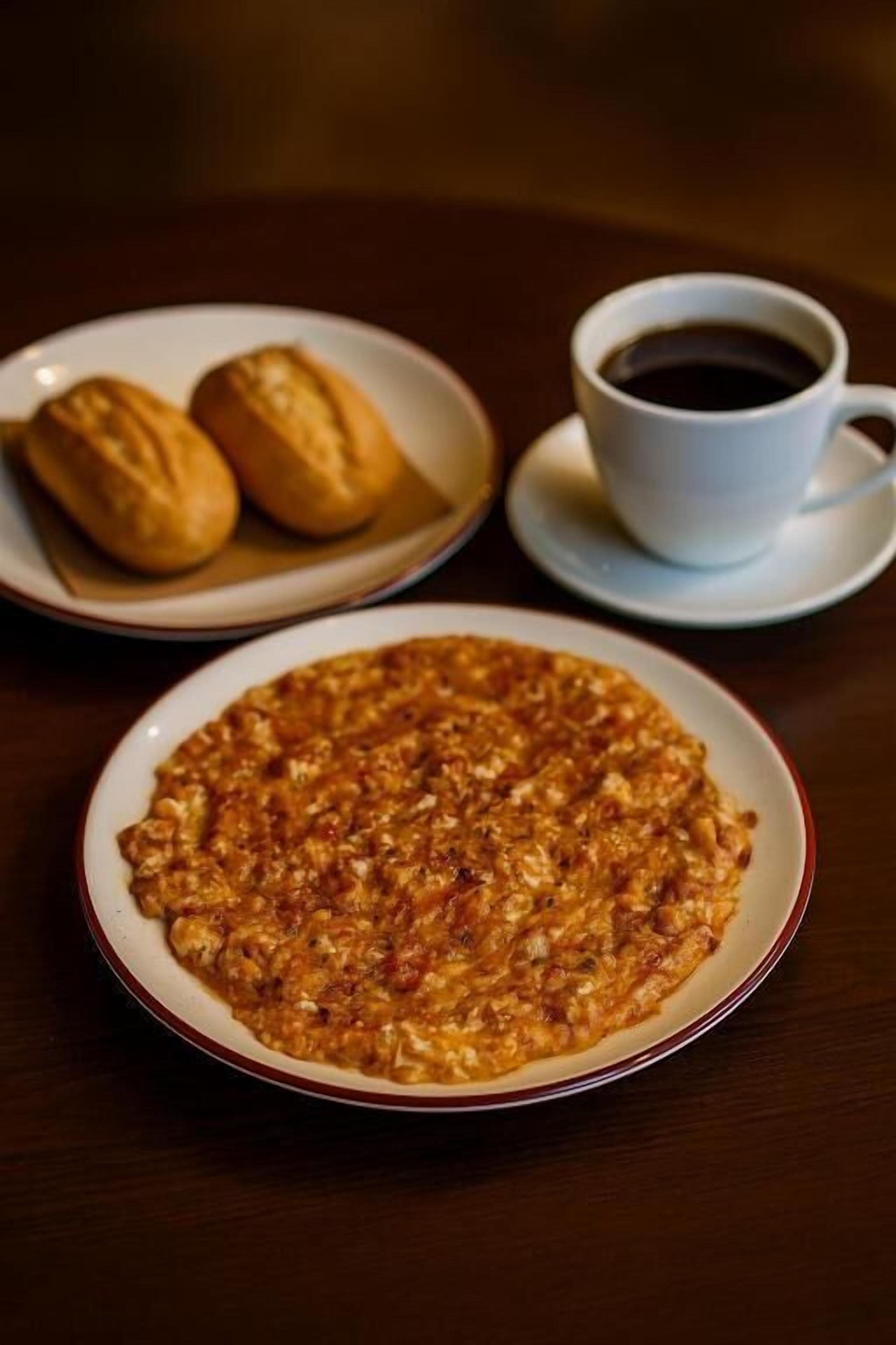 En tallrik med rörägg, en kopp kaffe och två bakverk på ett bord.