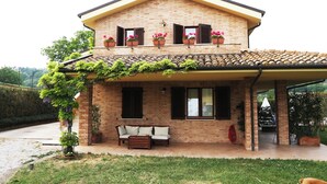 Uma casa de dois andares com fachada de tijolos, um alpendre com um sofá e plantas em vasos na varanda.