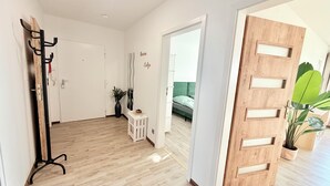 A hallway with a coat rack, a small table with a plant, and a wooden door with cutouts.