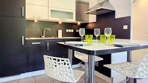 Een moderne keuken met donkere kastjes, een wit aanrecht en een ronde tafel met stoelen.