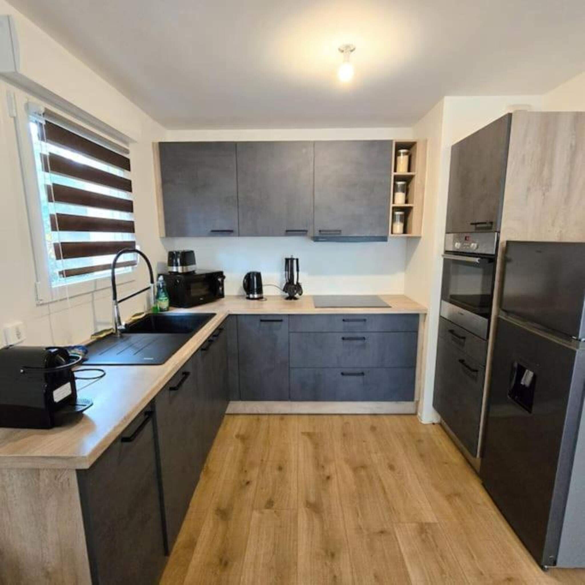 A compact kitchen with grey cabinets, a built-in oven, and a coffee machine.