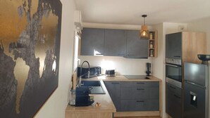 Moderni keittiö, jossa on harmaat kaapit, musta työtaso ja ruostumattomasta teräksestä valmistetut kodinkoneet.