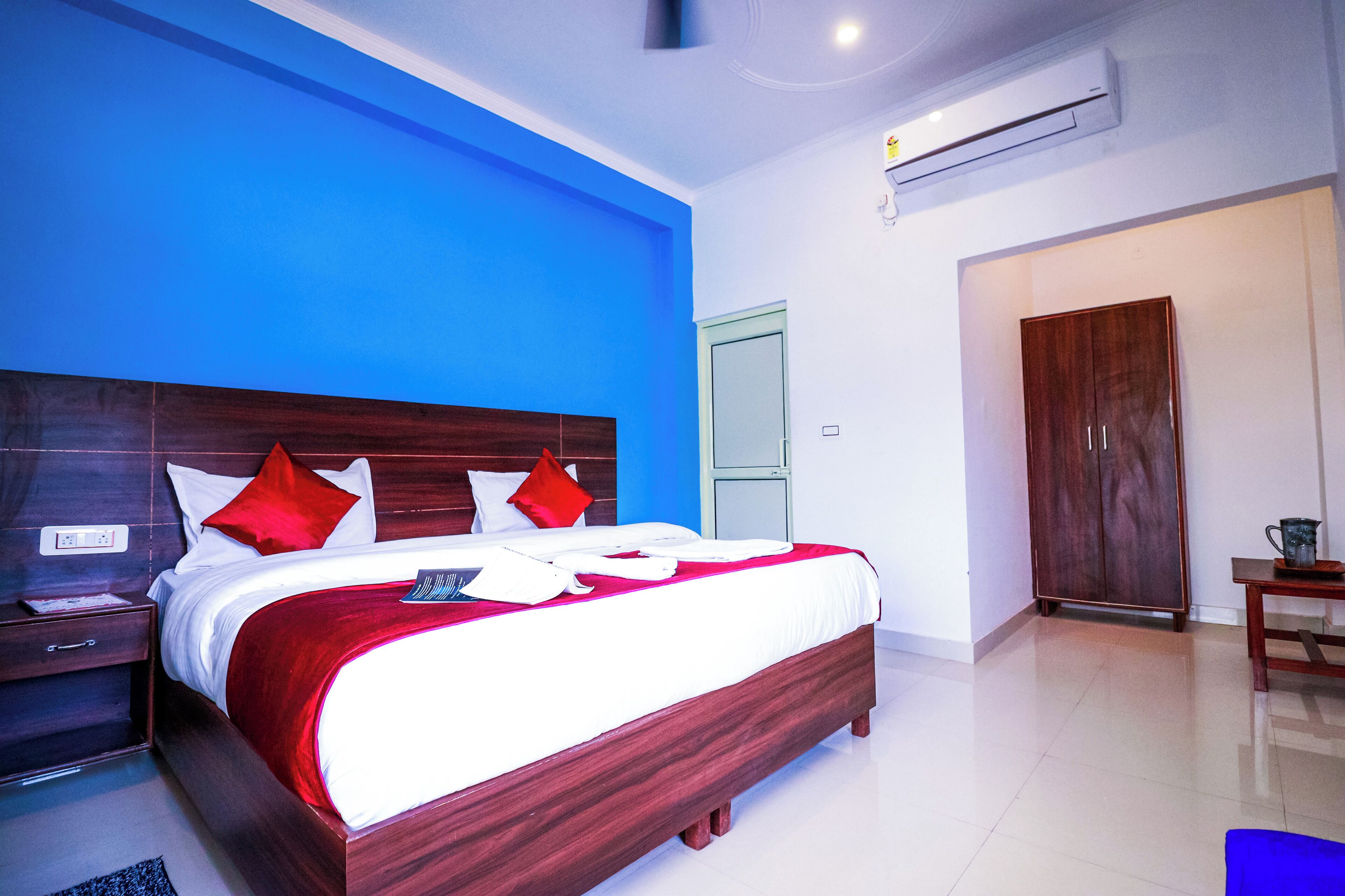 A hotel room with a large bed, a wooden headboard, a red and white bedspread, and a blue accent wall.