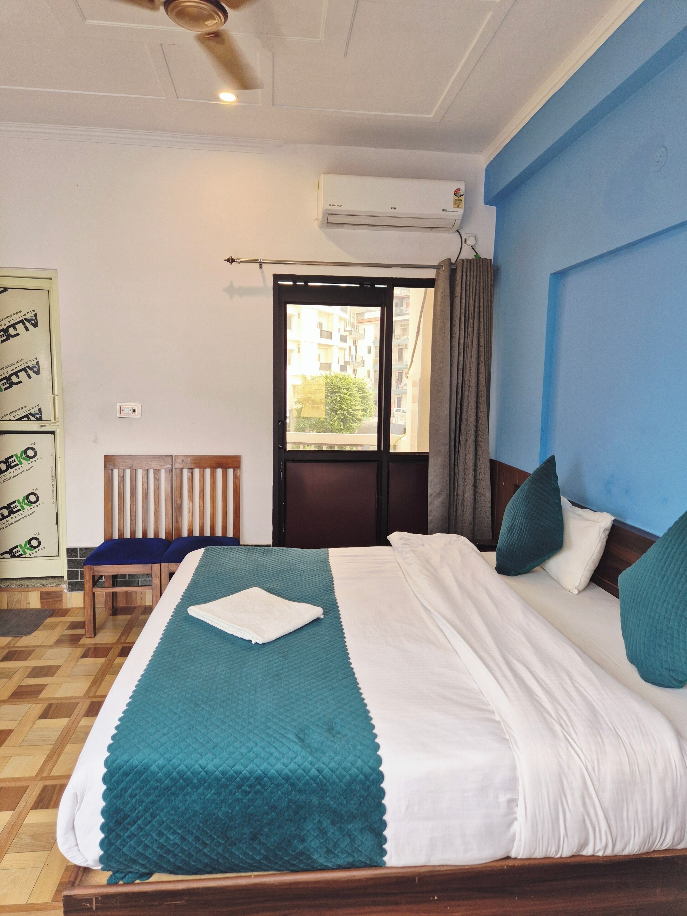 Una habitación de hotel con cama, una silla, un ventanal y un equipo de aire acondicionado.