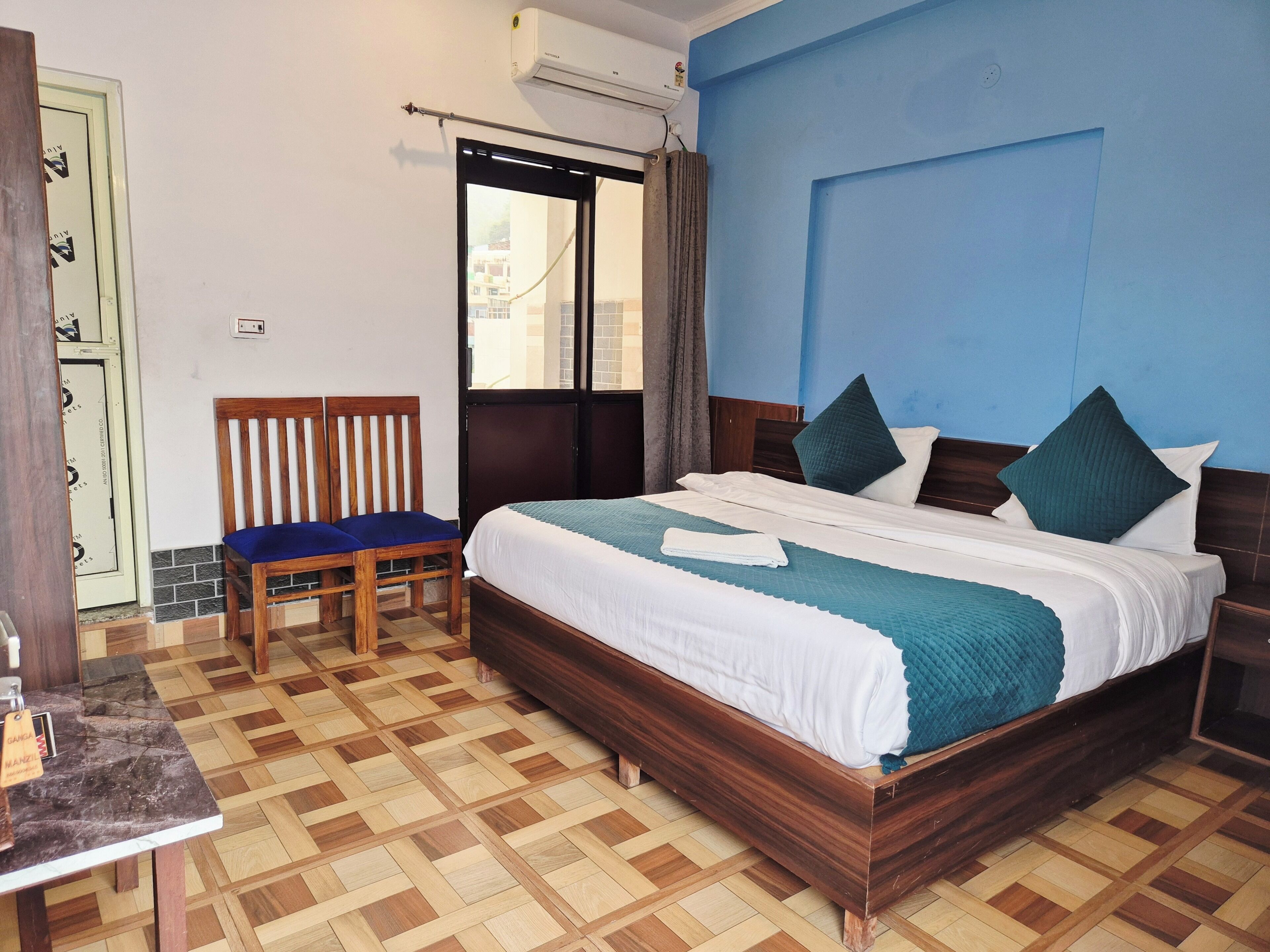 A hotel room with a bed, a chair, a small table, and a view through a window.