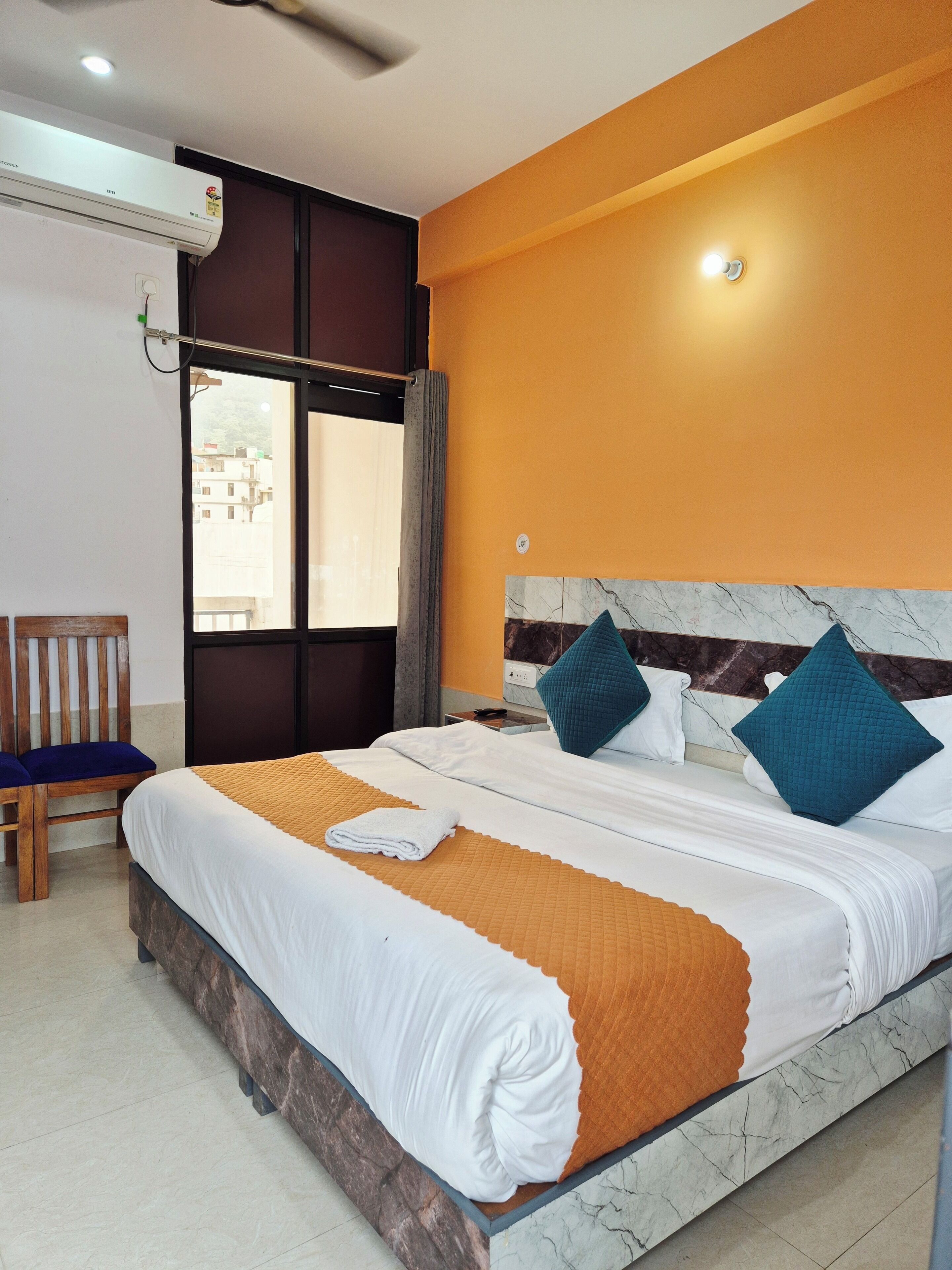 A hotel room with a bed, a chair, an air conditioning unit, a window, and a marble headboard.