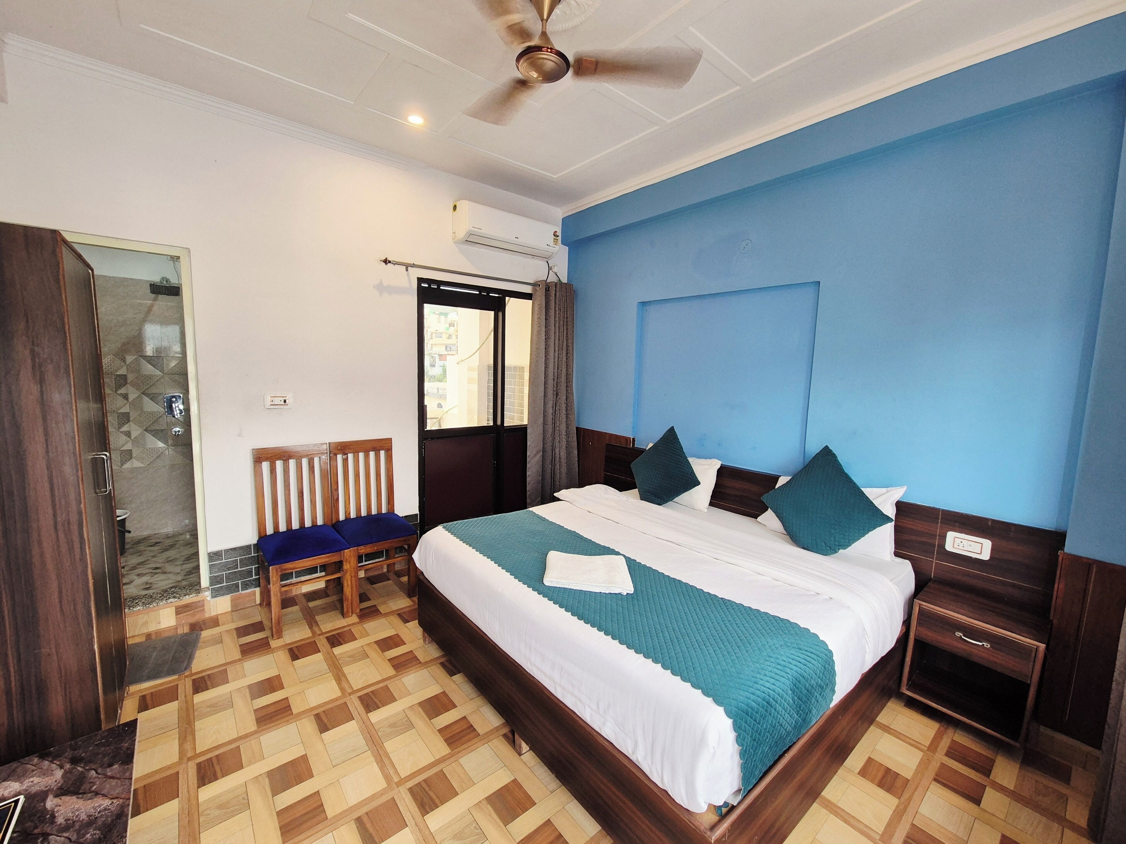 A hotel room with a bed, a wooden chair, a nightstand, a ceiling fan, and an air conditioning unit.