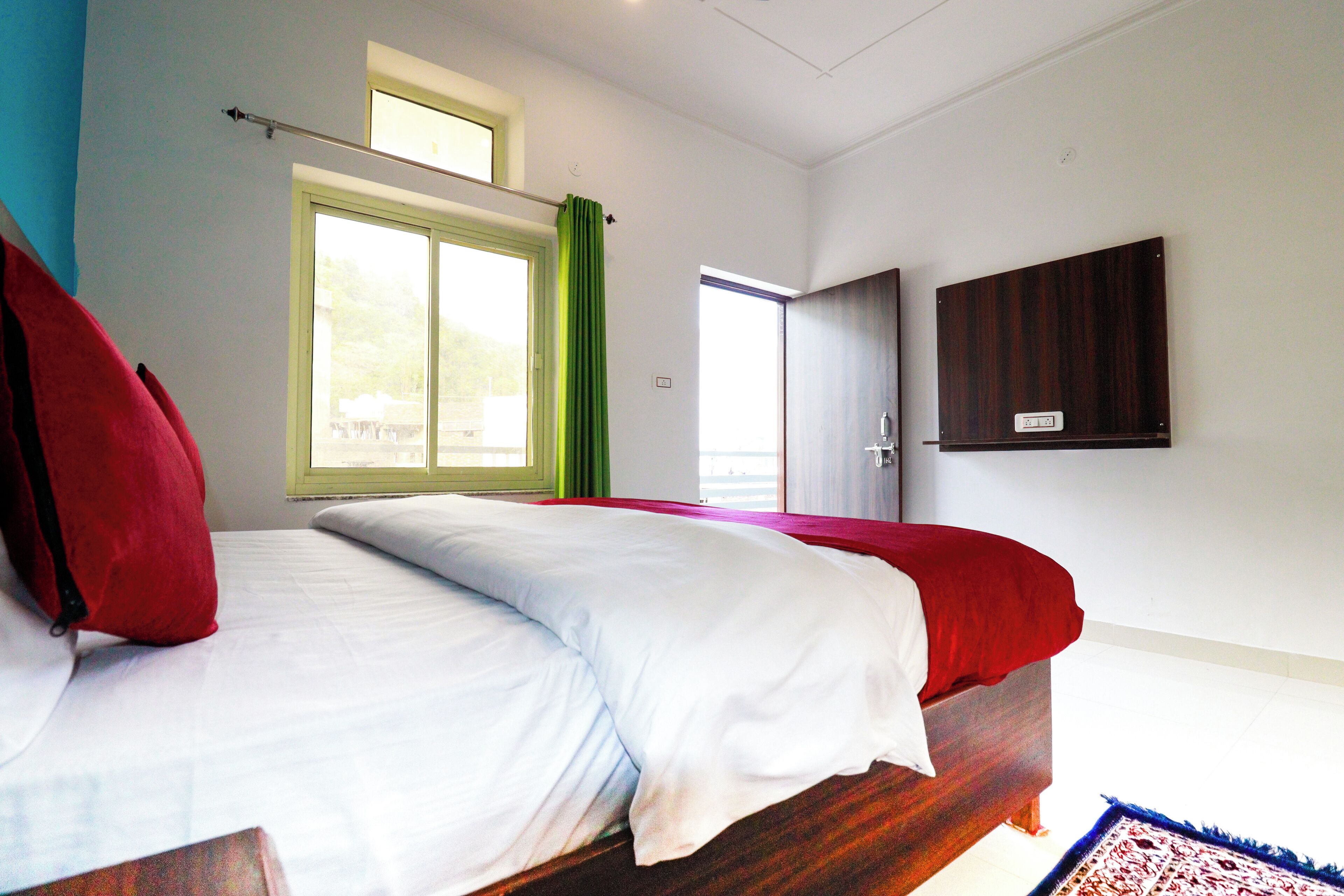 Une chambre à coucher avec un lit, une fenêtre avec des rideaux, une porte et un téléviseur fixé au mur.